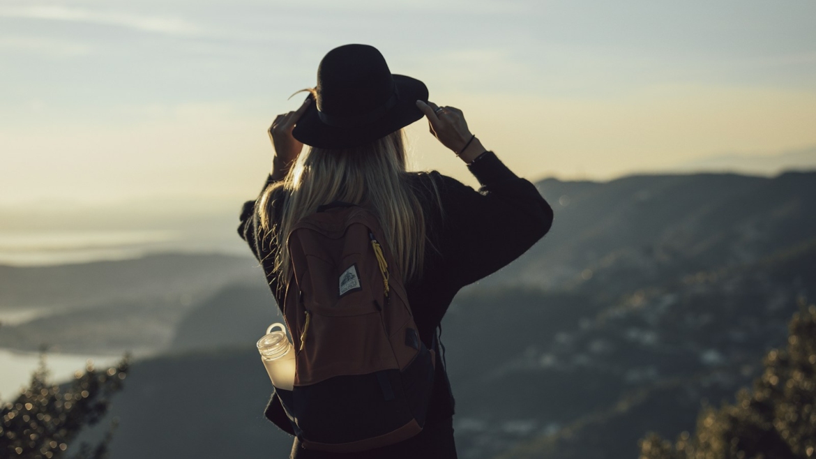 woman in gray hoodie and black pants wearing black hat standing on top of mountain during