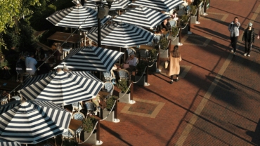 A group of people sitting under umbrellas on a sidewalk
