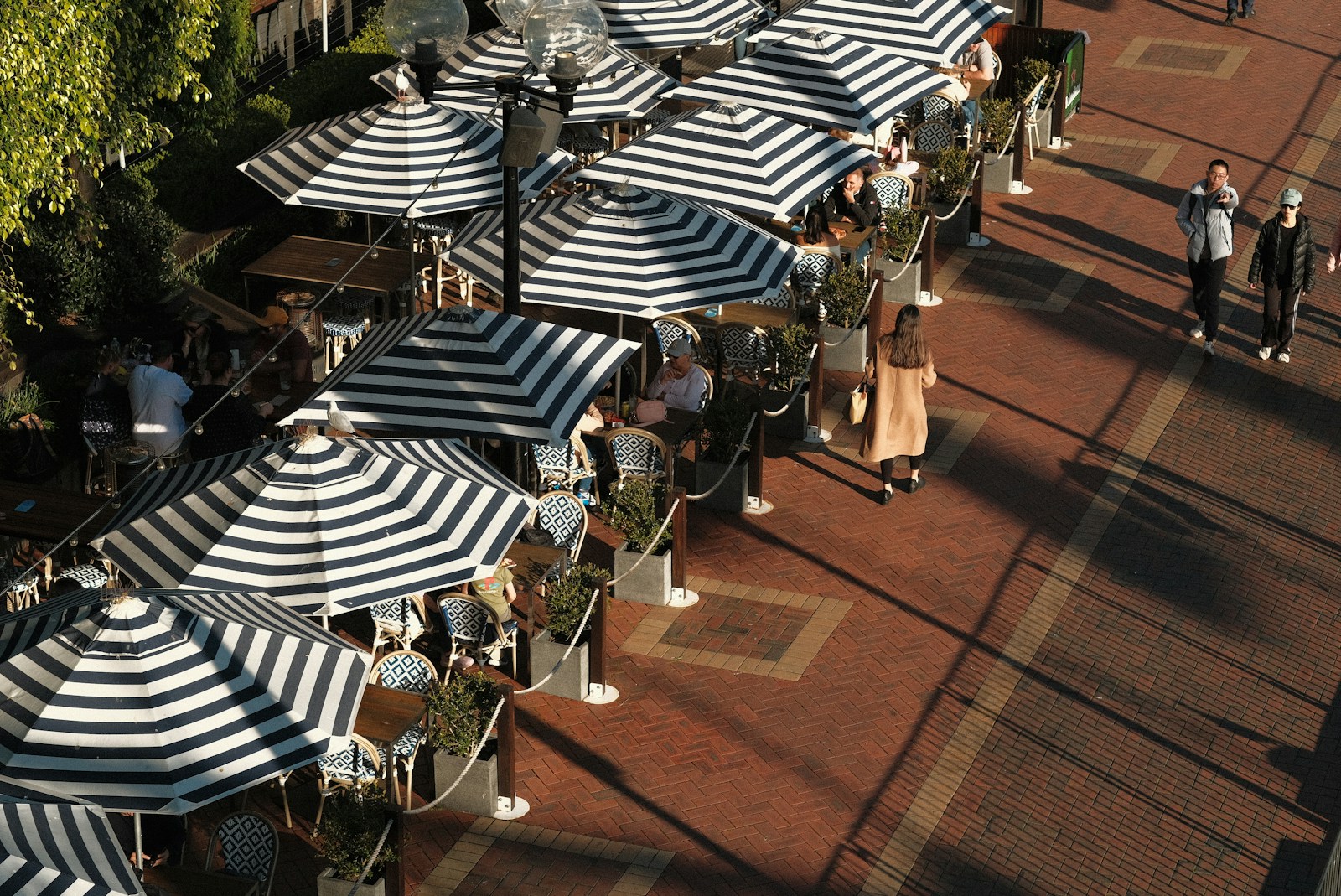 A group of people sitting under umbrellas on a sidewalk